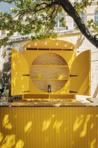 Bright yellow La Boule Bleue x InterContinental pop-up bar in the garden of the InterContinental Marseille Hôtel-Dieu, outdoor pétanque and apéritif space